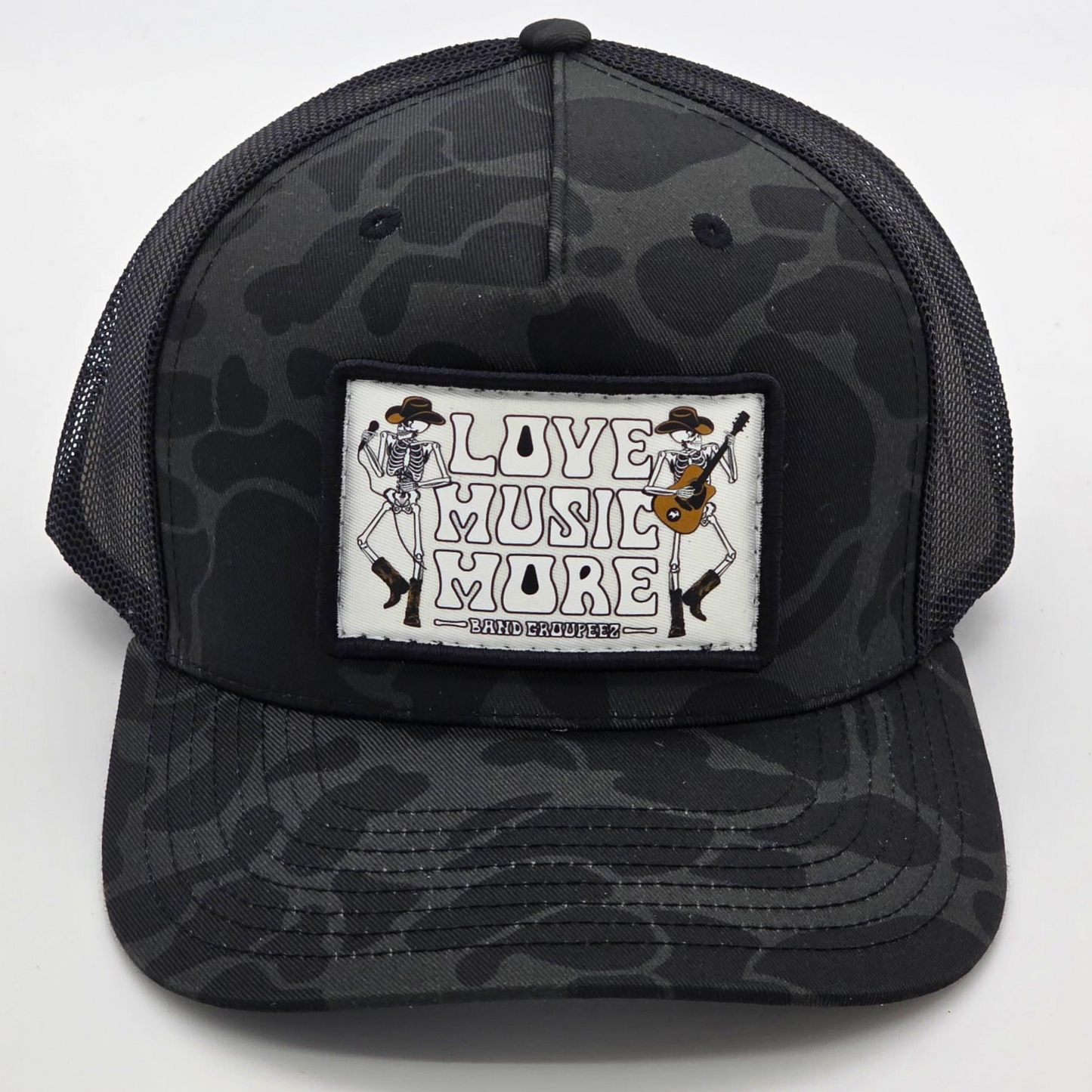 Black camouflage trucker hat with 'Live Music More' patch on a white background