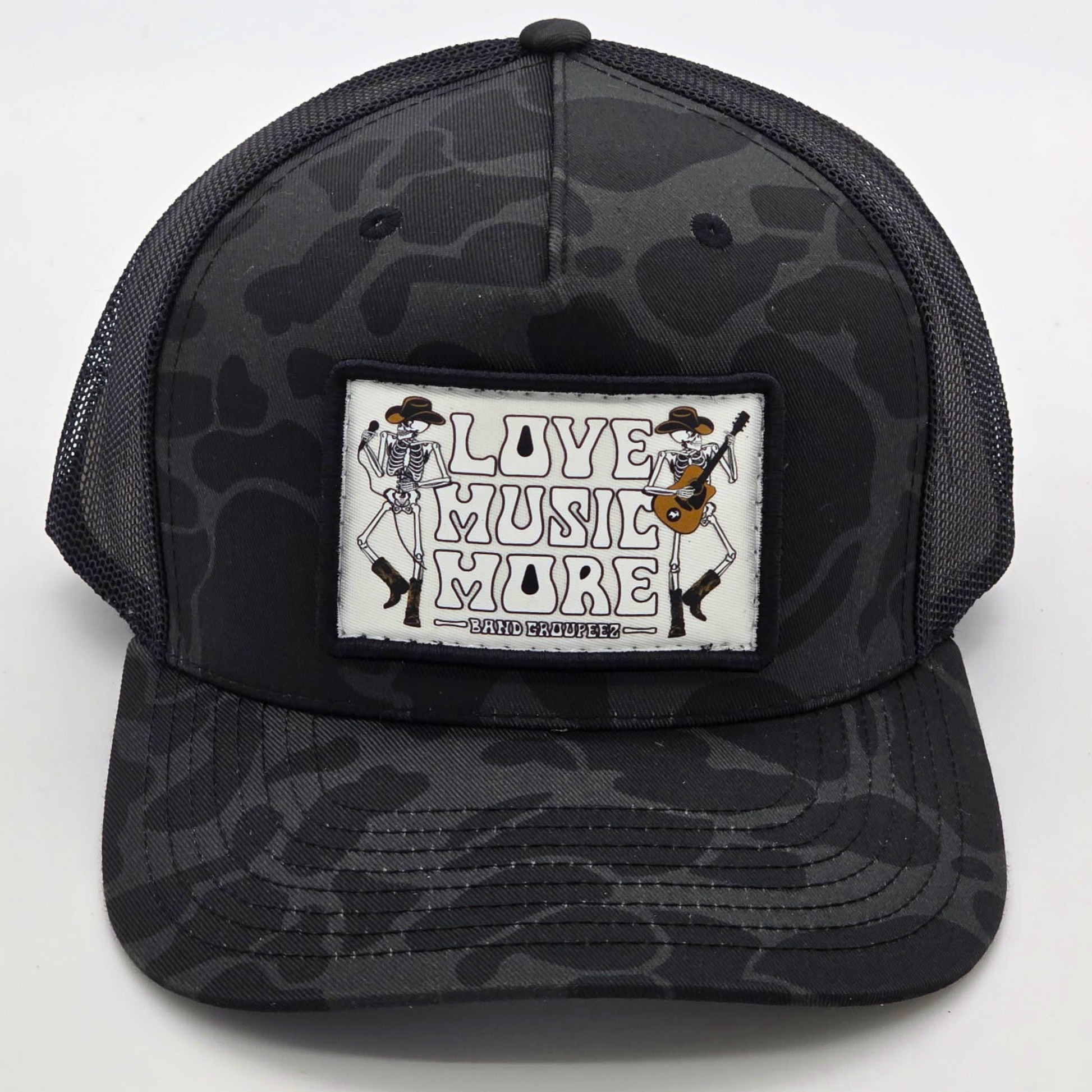 Black camouflage trucker hat with 'Live Music More' patch on a white background