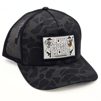 Black camouflage trucker hat with 'Live Music More' patch on a white background