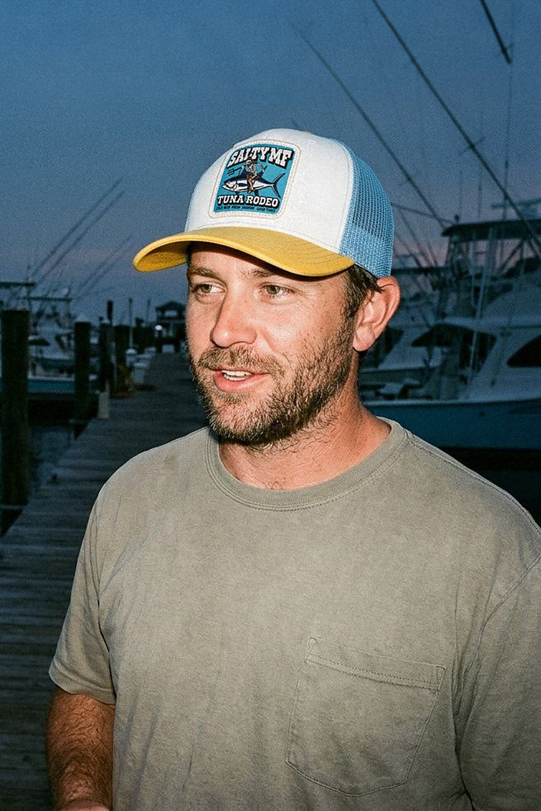 Man in a SALTY MF Tuna Rodeo trucker on a fishing dock at dusk