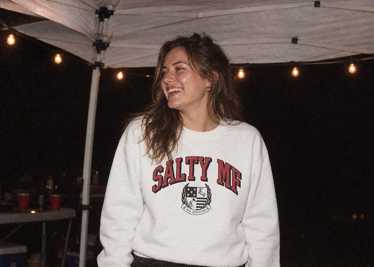 Woman in a SALTY MF crewneck under a tailgate tent at night
