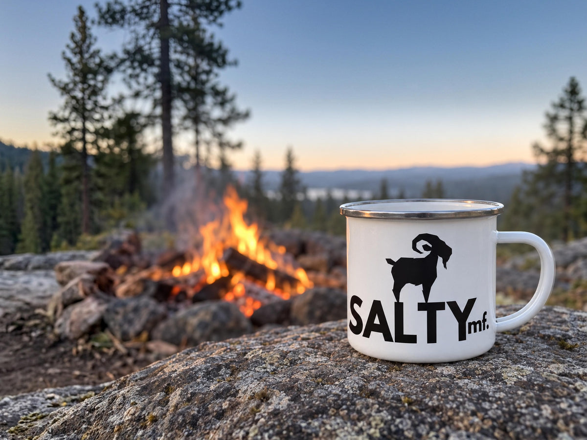 SALTYmf enamel camp mug on a granite rock beside a campfire at dusk