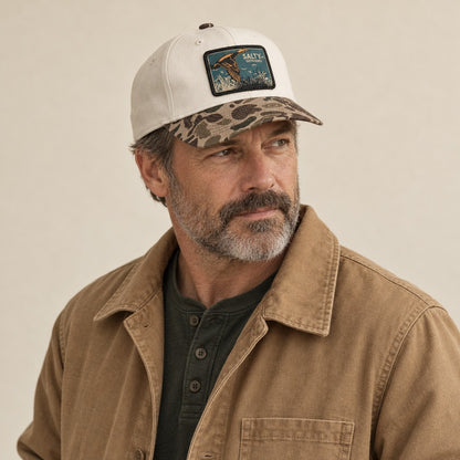 SALTYmf Duck Hunt Patch Gramps Hat in Cream/Bark Duck Camo, worn by a model, three quarter view with the woven SALTYmf Outdoors flying duck patch