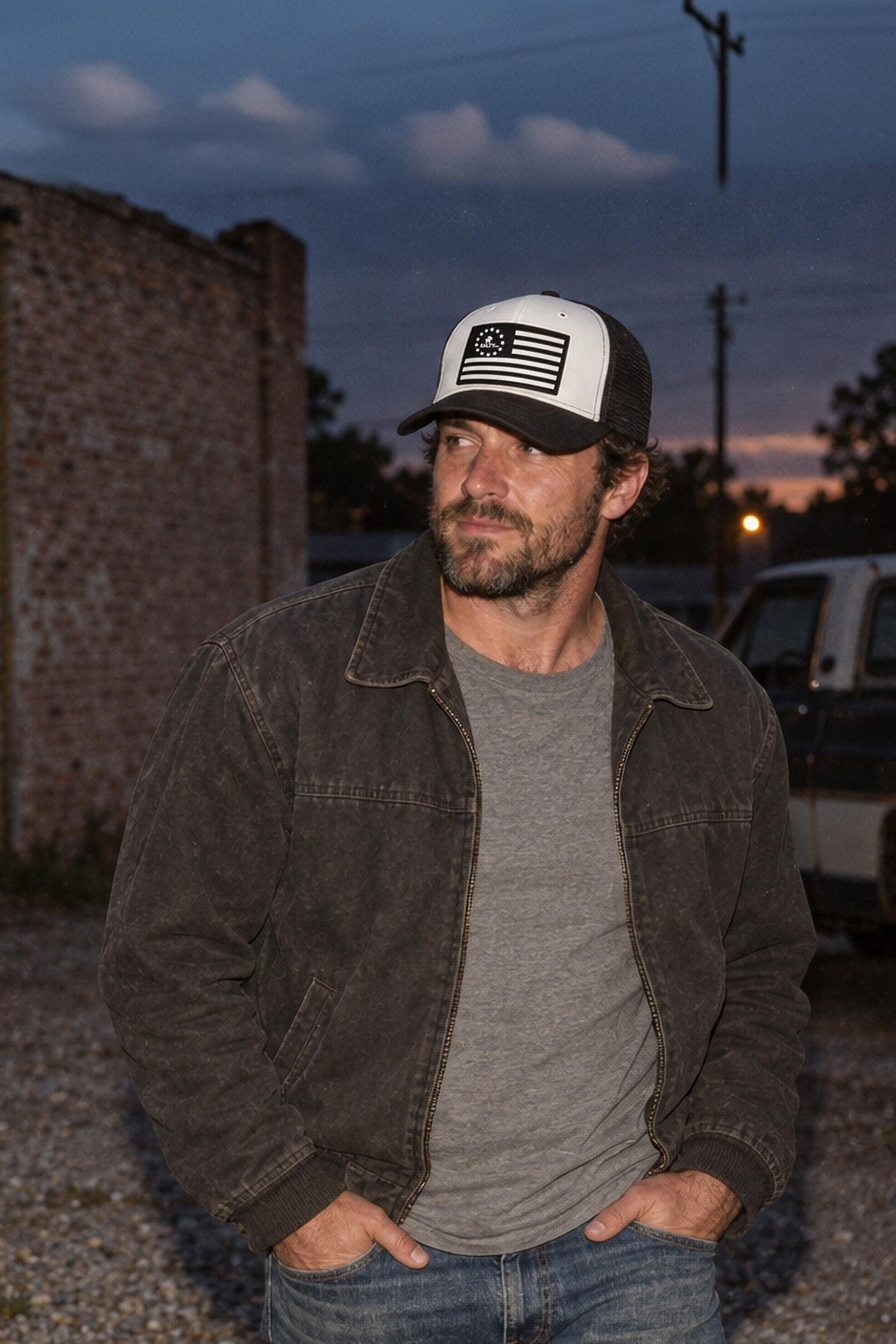 Man in the SALTYmf Ole Betsy trucker hat by a brick wall at dusk