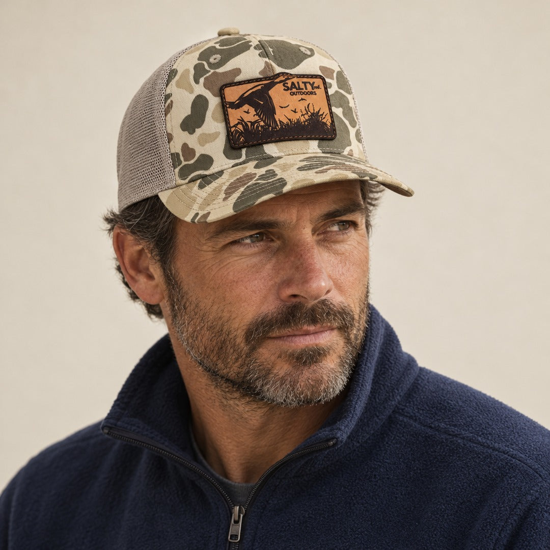 SALTYmf Leather Duck Hunt Patch Trucker in Harvest Duck Camo, worn by a model, three quarter view with the laser-etched leather duck patch