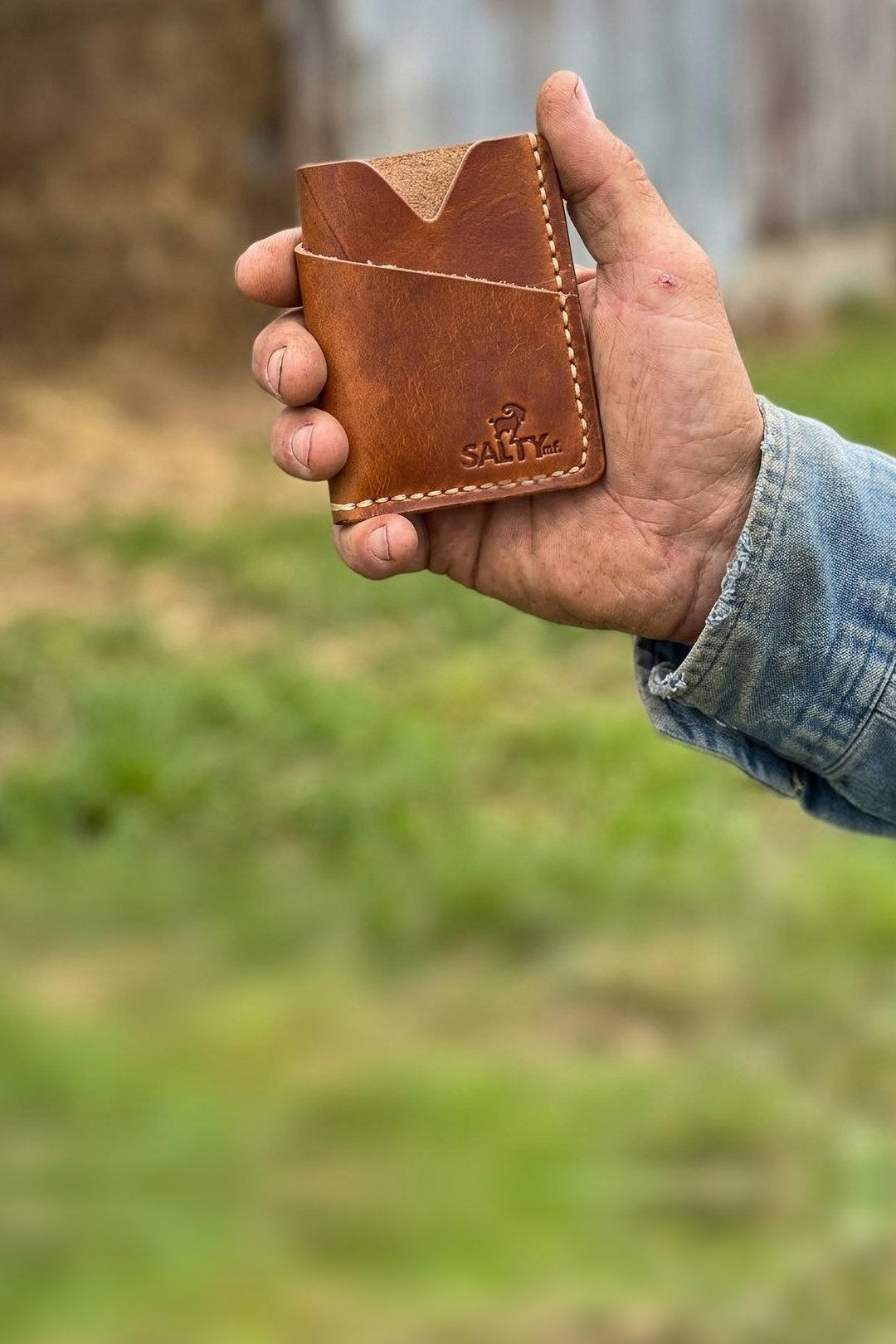 SALTYmf leather card holder wallet held in a working hand on a farm