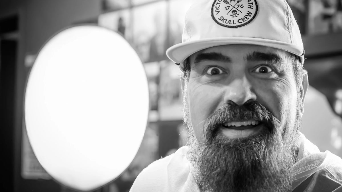 A bearded man in a Skull Crew cap makes a wide-eyed face at the camera